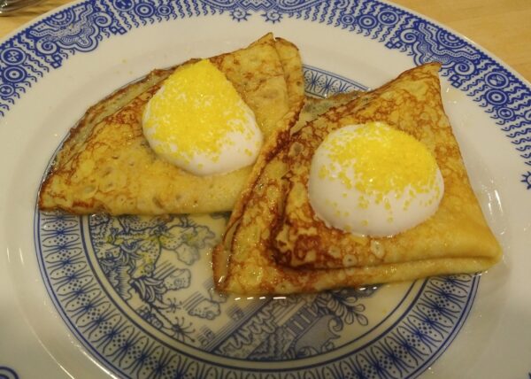 Two folded crepes on a plate, topped with whipped cream and yellow sprinkles