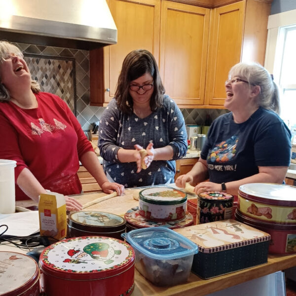 Three women laughing, heads back, while forming bread.