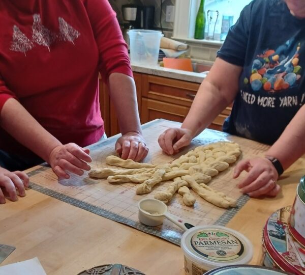 Two women plaiting a loaf of bread. Picture shows just their hands and the bread in progress.